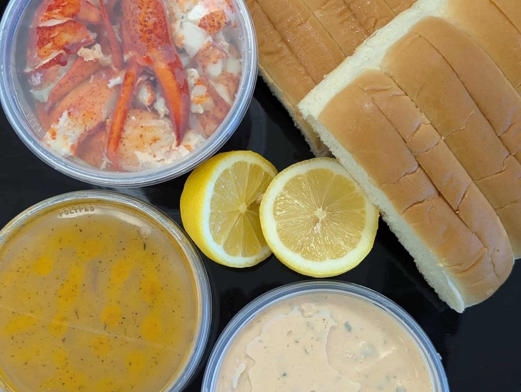 A lobster roll kit packed to go: claw and knuckle meat, split-top rolls, garlic butter, remoulade and lemons